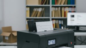 Scanner corporativo de alimentação automática digitalizando prontuário médico em arquivo organizado de clínica, com pastas suspensas e monitor de gestão documental ao fundo